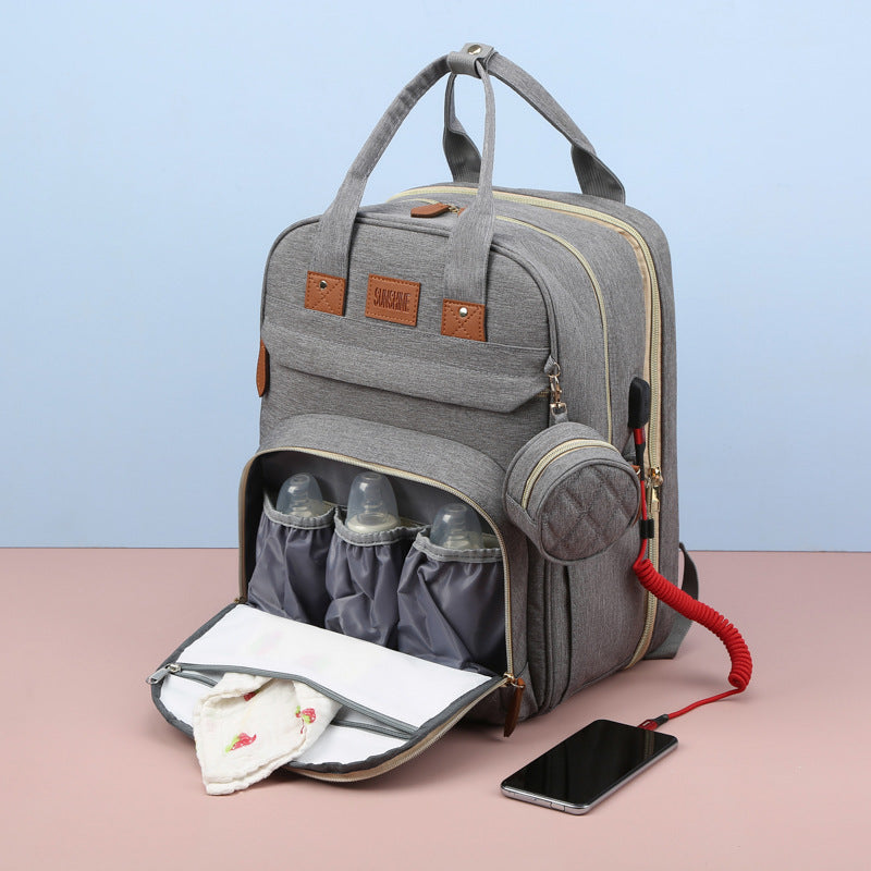 Gray diaper bag with bottles, wipes, and a phone on a pink surface with a light blue background