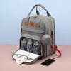 Gray diaper bag with bottles, wipes, and a phone on a pink surface with a light blue background