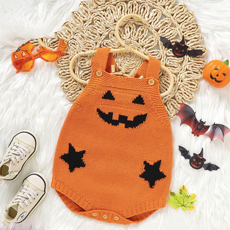 Orange knitted baby romper with jack-o'-lantern face design on a textured surface with Halloween decorations.