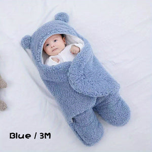 Baby wrapped in a blue fluffy blanket with bear ears on a white background