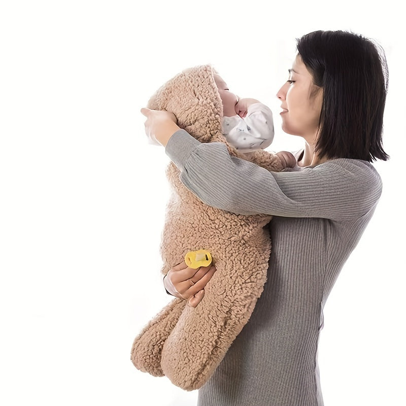 Mom holding a baby wrapped in a brown fluffy swaddle with a teddy bear on a white background