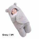 Baby wrapped in a gray fleece swaddle with bear ears on a white background