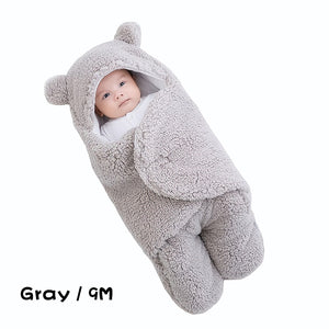 Baby wrapped in a gray fleece swaddle with bear ears on a white background