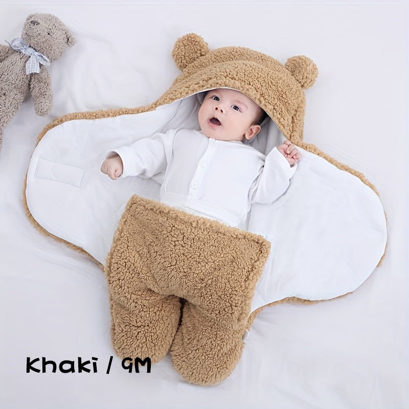 Baby in a beige bear-themed outfit with a white blanket, lying on a light gray surface.