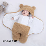 Baby in a beige bear-themed outfit with a white blanket, lying on a light gray surface.