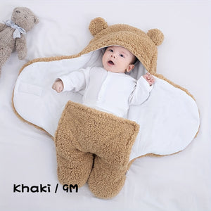 Baby in a beige bear-themed outfit with a white blanket, lying on a light gray surface.