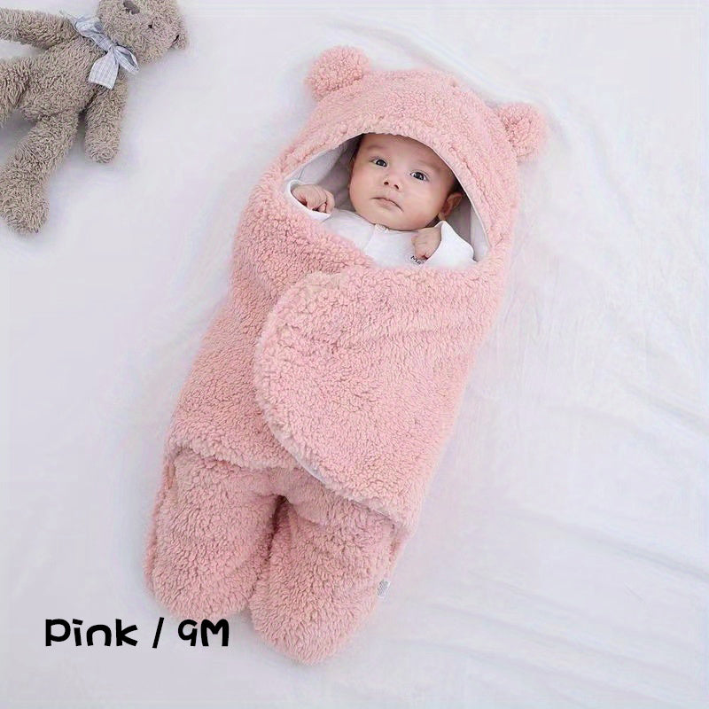 Baby wrapped in a pink fluffy swaddle with bear ears on a white background