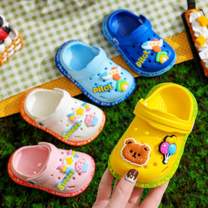 Colorful children's clogs with cartoon designs on a green checkered fabric background.
