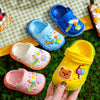 Colorful children's clogs with cartoon designs on a green checkered fabric background.