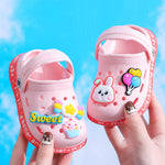 Pink children's sandals with cartoon designs held against a blue background