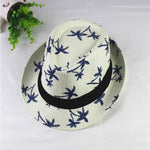 White straw hat with blue floral patterns and a black band on a light gray background.