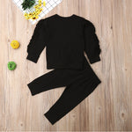 Black long-sleeve top and pants set on a wooden surface with decorative items.