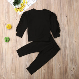Black long-sleeve top and pants set on a wooden surface with decorative items.