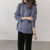 Person wearing a blue sweater and black pants against a white wall.