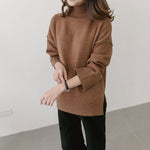 Person wearing a brown sweater and black pants against a white wall.
