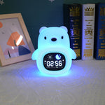 Colorful bear-shaped alarm clock on a surface with books and a framed picture in the background.