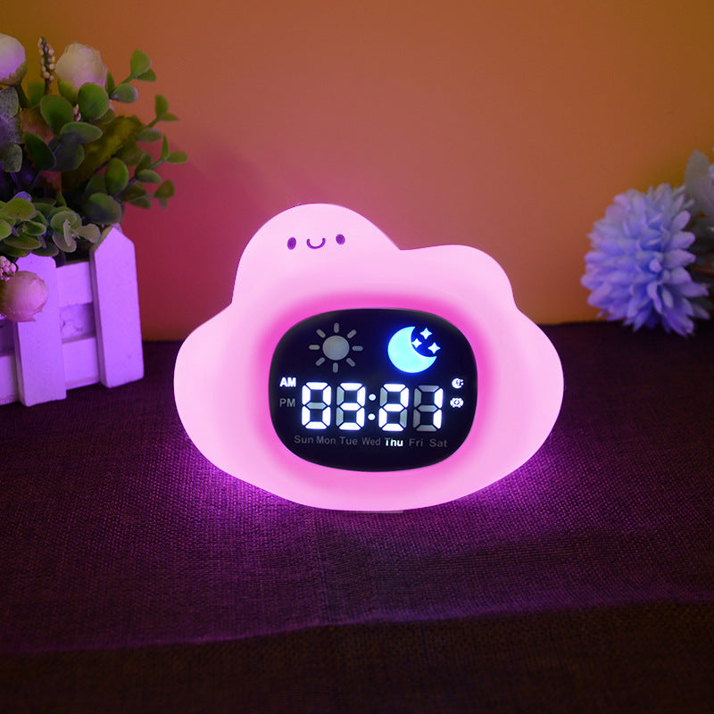 Digital clock with a pink cloud design on a dark surface with flowers in the background