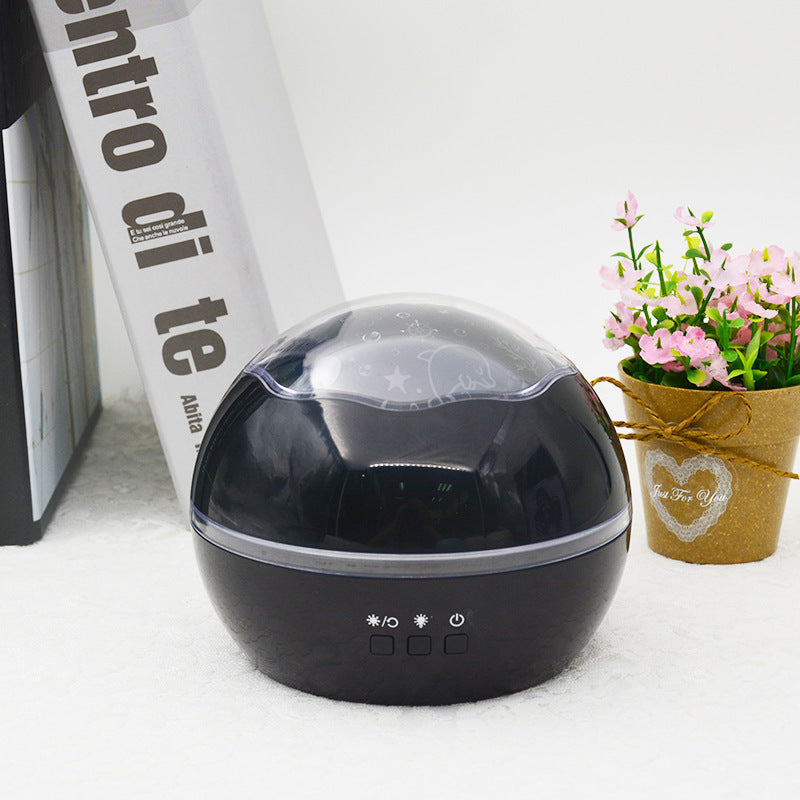 Black spherical device with control buttons on a white surface next to a book and small potted plant.