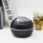 Black spherical device with control buttons on a white surface next to a book and small potted plant.