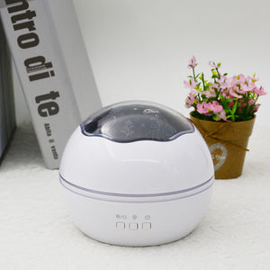 White spherical device with a dark top on a light surface, next to a book and small potted plant.