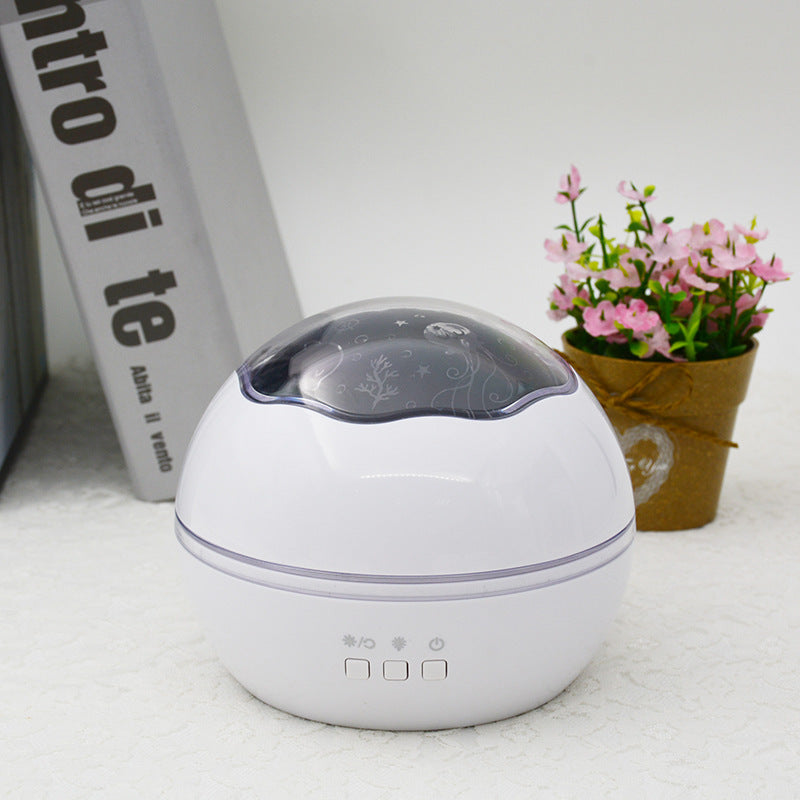 White spherical device with a dark top on a light surface, next to a book and small potted plant.