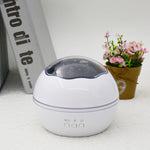 White spherical device with a dark top on a light surface, next to a book and small potted plant.