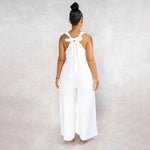 Woman wearing a white jumpsuit with a bow detail on the back against a plain background