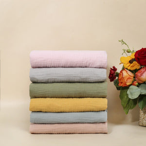 Stack of colorful folded fabrics with a vase of flowers on a beige background