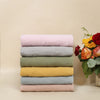 Stack of colorful folded fabrics with a vase of flowers on a beige background