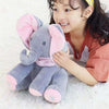 Child holding a gray elephant plush toy with pink ears and trunk on a soft surface