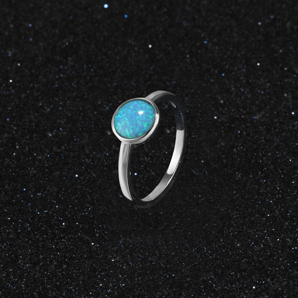 Silver ring with a blue opal stone on a black sand background