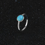 Silver ring with a blue opal stone on a black sand background