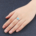 Hand wearing a silver ring with a blue gemstone on a dark textured background