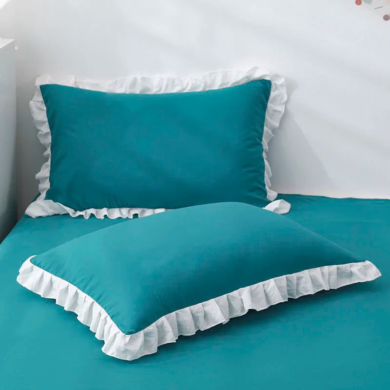 Blue pillows with ruffled edges on a bed in a bedroom setting.