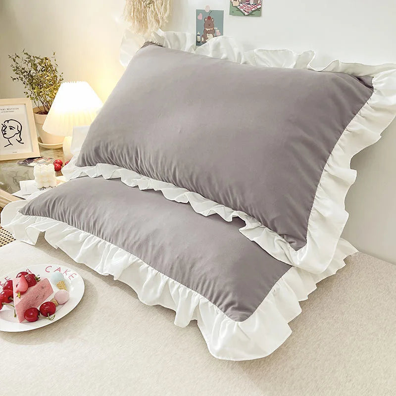 Gray pillows with ruffled edges on a bed in a bedroom setting.