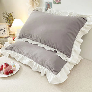 Gray pillows with ruffled edges on a bed in a bedroom setting.