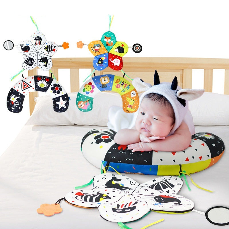Baby in a cow costume surrounded by colorful baby toys on a crib