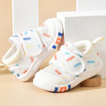 White children's sandals with colorful accents on a beige surface