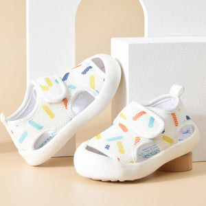 White children's sandals with colorful patterns on a beige surface